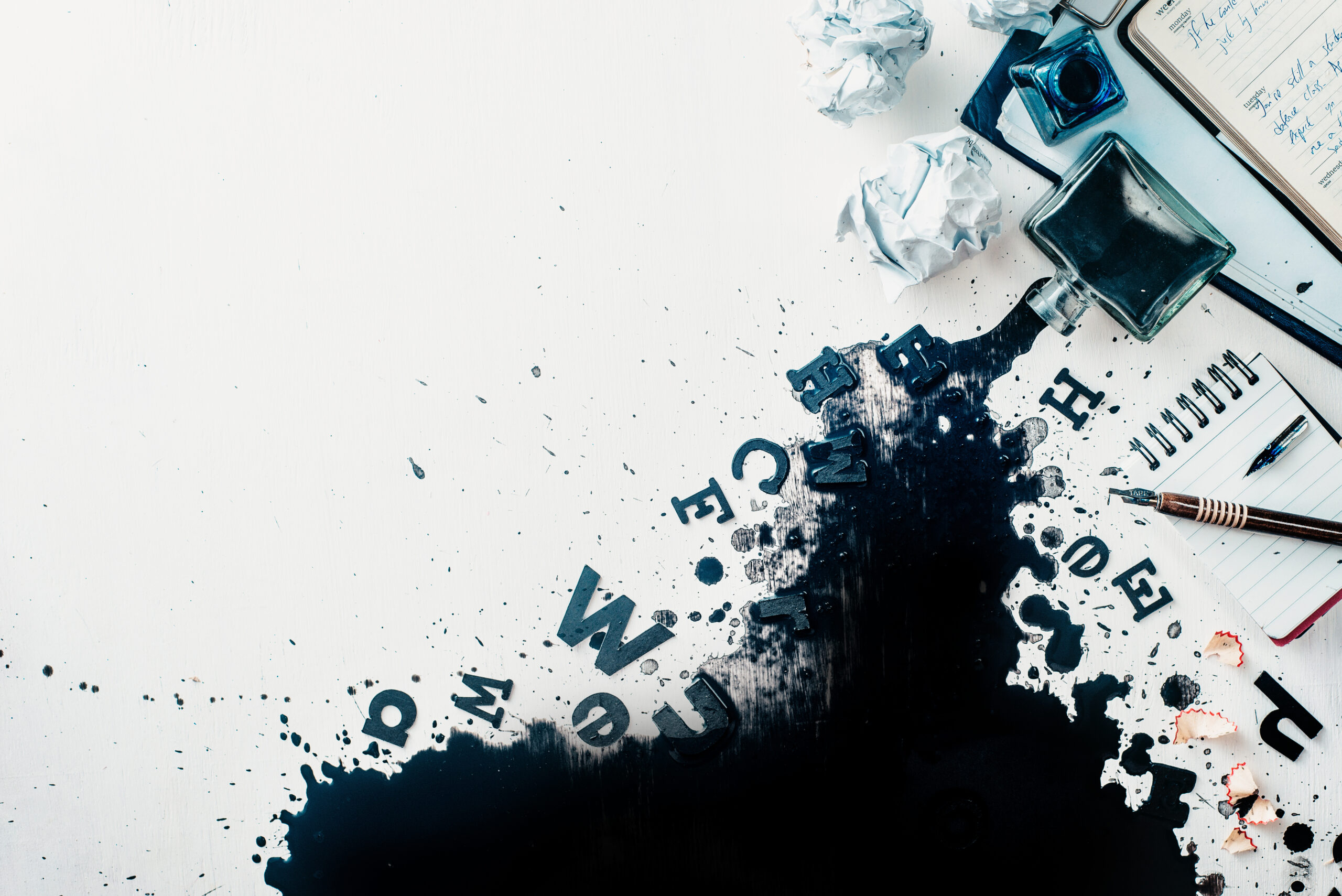 Header with spilled ink, crumpled paper, scattered letters, papers and notepads on a white wooden background. Creative writing concept. Flat lay with copy space.
